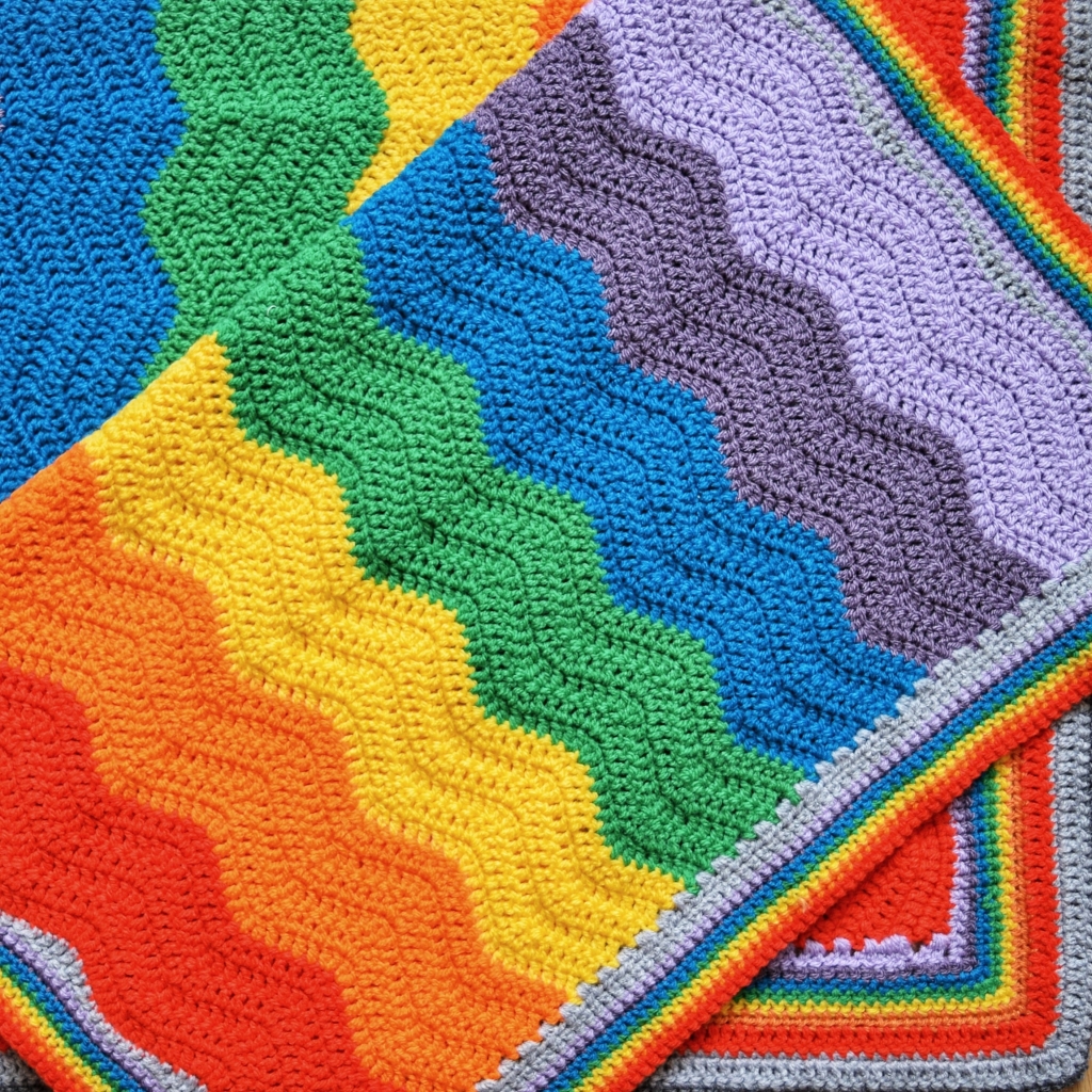 Two crocheted rainbow coloured blankets laid flat